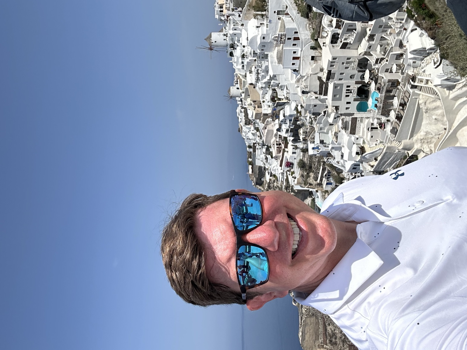 Eric, smiling in sunglasses on a hillside above a white cliffside village.