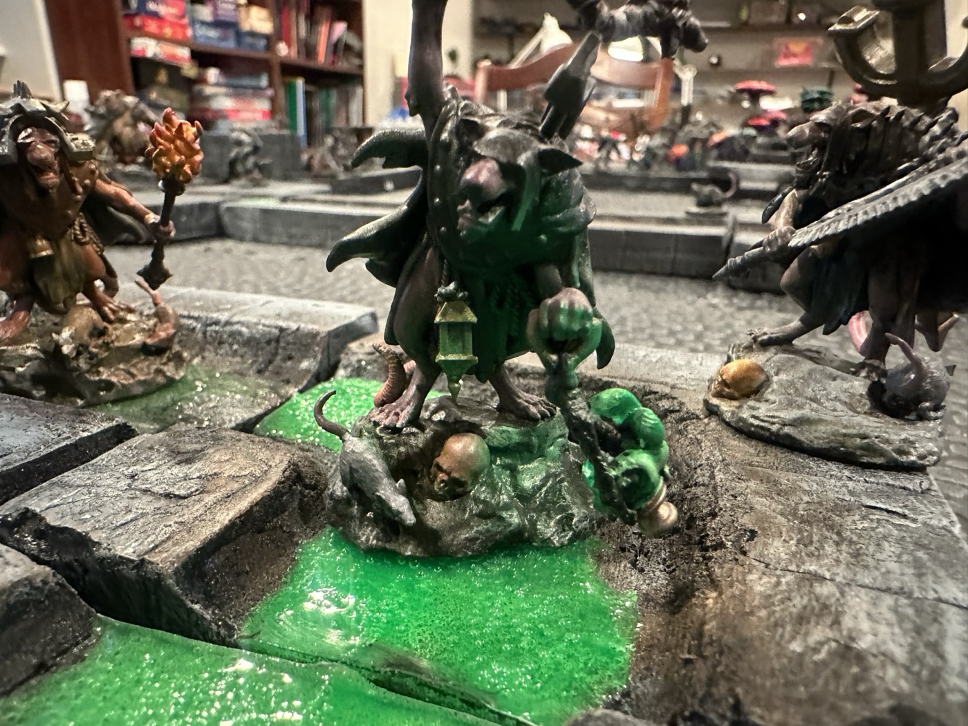 A painted wererat miniature holding a lantern, standing over a skull in a glowing green sewer.
