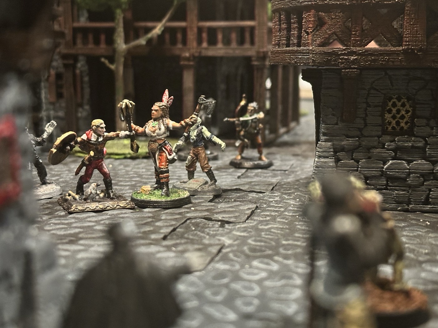 Four painted adventurer miniatures on a cobblestone street, weapons drawn, between timber buildings.